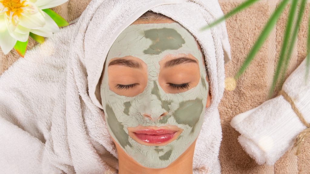 Frau mit grüner Gesichtsmaske und Handtuchturban bei Kosmetikbehandlung