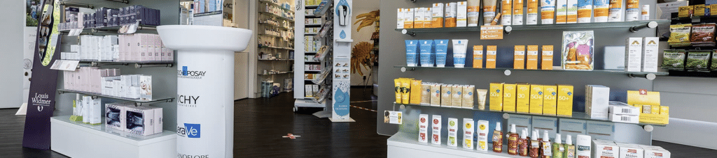 Innenraum der Kloster Apotheke mit hellen Regalen, gefüllt mit Hautpflege- und Sonnenschutzprodukten verschiedener Marken, auf dunklem Bodenbelag
