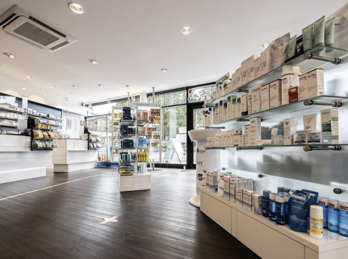 Innenaufnahme der Apotheke mit weißen Regalen, dunklem Boden und modernen Lichtspots an der Decke