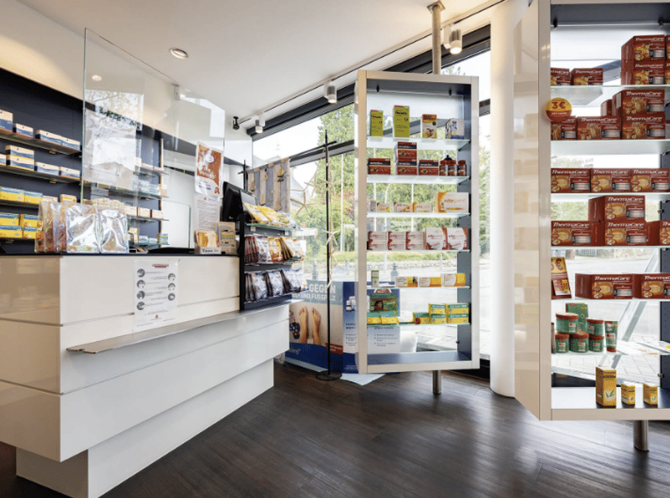 Verkaufsbereich der Apotheke mit hellen Regalen und bodentiefen Fenstern, gefüllt mit Medikamenten und Gesundheitsprodukten