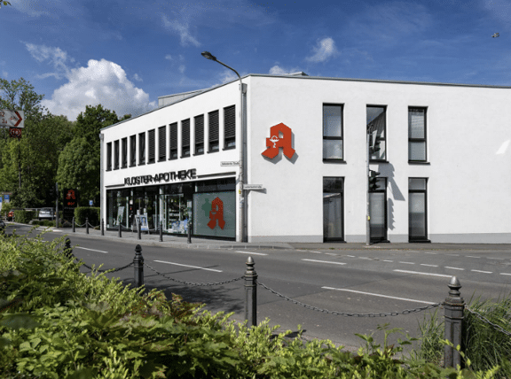 Fassade der Kloster Apotheke mit großen Glasfenstern und Eingangstür, spiegelt Straßenansicht wider