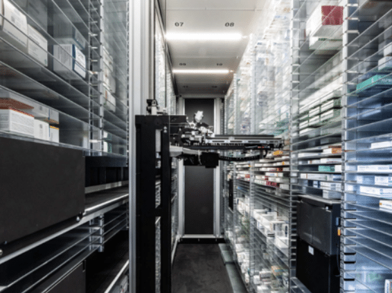 Automatisches Lagersystem einer Apotheke mit Regalen voller Medikamentenschachteln und einem Roboterarm zur Ausgabe